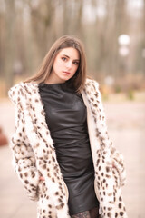 Portrait of a young beautiful dark-haired girl in a fur coat in nature.