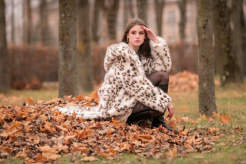 Portrait of a young beautiful dark-haired girl in a fur coat in nature.