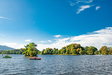 Scenic view of an island in the middle of Lake Ammersee with lush green trees and a blue sky with fluffy clouds. Ideal for travel brochures, postcards, and travel websites