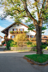Traditional Bavarian house with wooden balconies decorated with vibrant pink flowers, set against a blue sky. Picturesque architecture in Ammersee, Bavaria, Germany.