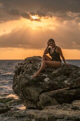 Woman Sunset Beach - Silhouette of woman sitting on a rock at sunset with the ocean behind her.