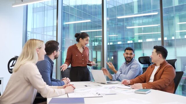 Young female employee giving a successful presentation to a group of business people on conference in meeting room. Speaker presenting a project. Team praises colleague for excellent report applauding