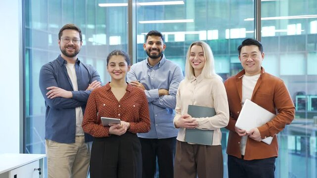 Portrait of group happy multiethnic team standing in modern office. Successful corporate colleague workers posing looking at camera smiling. Teamwork of confident professional leaders and employees