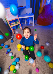 Obraz premium Child plays happily with balls. A young child sits on a soft carpet, surrounded by colorful balls, laughing and enjoying the playful indoor atmosphere.