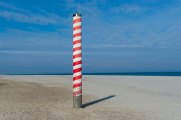 Striped Navigation Pole on a Sandy Beach with Blue Sky and Sea in Jastrzębia Góra