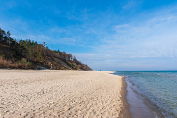 Golden Sandy Beach with Gentle Waves and Forested Cliffs on a Sunny Day in Jastrzębia Góra