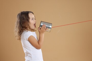 Girl using tin can telephone on beige background