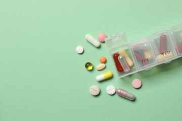 Plastic container with various pills on green background