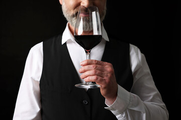 Professional sommelier tasting red wine on black background, closeup