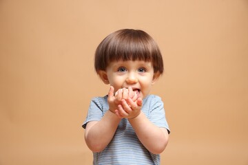 Cute little child eating tasty mochi on light brown background