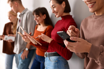 Group of people using different gadgets near light wall indoors. Modern technology