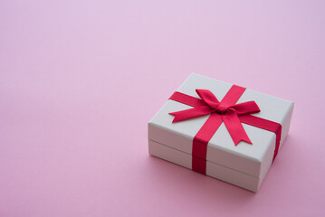 White gift box with red bow ribbon on pink background copy space. Present box for giving in anniversary, celebration, festival and abstract reward symbol in business concept.