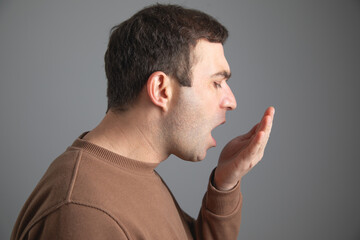 Man checks his breath with his hand. The concept of halitosis