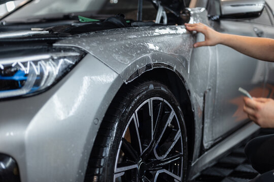 Professional man covers a car with protective film in a detailing center. Car protection and care