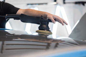 Professional man with polishing tool polishing car in garage . Detailing. Varnish care and scratch removal