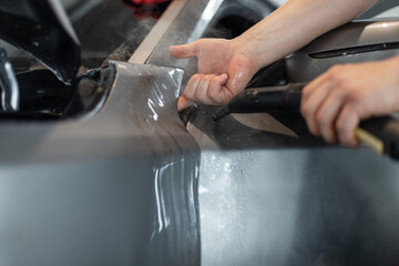 professional man will cover a car with protective PPF film at a detailing service.