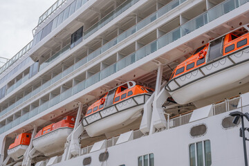 Large cruise ship with lifeboats docked at port, showing safety equipment and balcony cabins. Orange emergency passenger life boats on a white modern cruise liner, side view