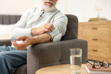 Senior man measuring blood pressure in armchair at home, closeup