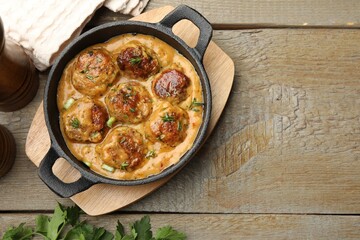 Delicious meatballs with gravy cream sauce and herbs on wooden table, flat lay. Space for text