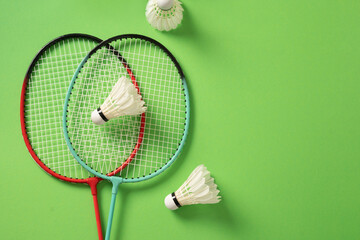White feather badminton shuttlecock and badminton racket on green background. View from above. Concept racket sport. Leisure games.