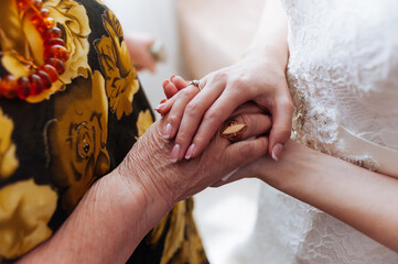 A close-up of the bride's hand, adorned with a wedding ring, holding the hand of an elderly woman,...