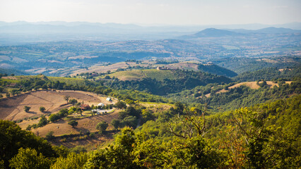 Naklejka premium Scenic view to the countryside of Tuscany with small fields, deep woods, hills and small farms offers typical view to the italian countryside during hot summer day and evokes beauty of local nature.