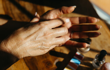 Close-up of female hands applying hand cream on a wooden table