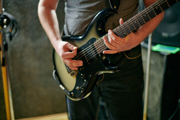 Obraz premium Musician playing an electric bass guitar at music rehearsal, practicing guitar technique in dimly lit setting, close up view guitarist hands