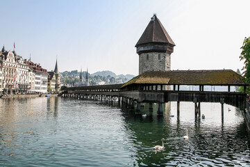 A bridge over a body of water with a building in the background in Lucerne Switzerland. The bridge is wooden and has a roof