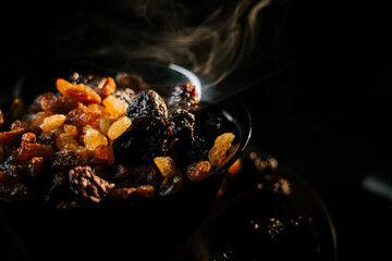 Various raisins in a black bowl with smoke rising, creating a warm and inviting atmosphere in a cozy kitchen at dusk