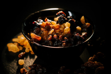 Raisins and dried fruits in a black bowl illuminated by soft light creating rich textures