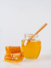 Glass jar full of honey and wooden dipper with honey drop isolated on white background