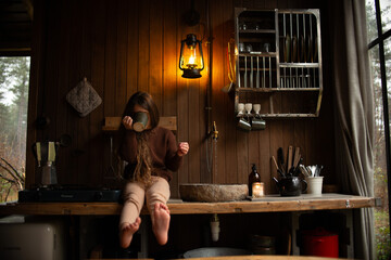little girl sitting on kitchen table with cup in forest house