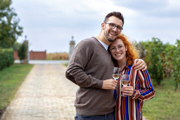 Young couple with glass of vine in hands hug and smile in vineyard