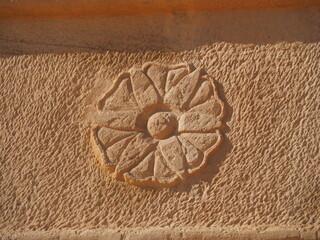 A close-up shot of a Nabataean rosette, intricately carved into a rock face in Madain Saleh, Saudi...