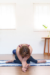 Senior Asian woman performing Janu Sirsasana Head to Knee Forward Bend on a yoga mat in a peaceful...
