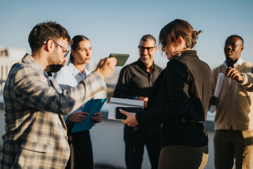 Fototapeta premium A group of multicultural business colleagues gather on a rooftop at sunset, celebrating a successful achievement with smiles and enthusiasm.