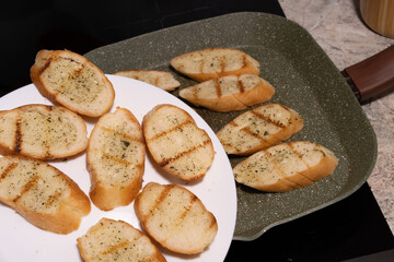Slices of toasted bread, likely garlic bread, on a white plate and in a green frying pan