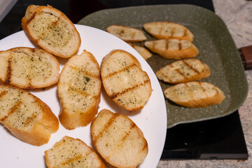 Slices of toasted bread, likely garlic bread, on a white plate and in a green frying pan