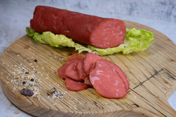 Vegan salami sausage made with washed  flour and bits og vegan cheese fat, sliced on wooden board