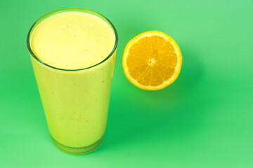 A glass of avocado smoothie with a lemon on the side. The lemon slice is cut in half and placed on a green table