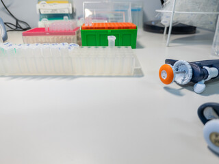 Plastic rack with eppendorf tubes in a laboratory on a working bench.  Some boxes with micropipette tips in the background. Background for science, DNA analysis. Micropipettes are partially visible.