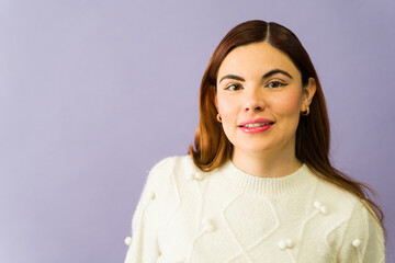 Fototapeta premium Cheerful young woman smiling and wearing a white sweater on a purple background