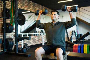 Middle aged man working out with dumbbells in gym, lifting weights while sitting on bench