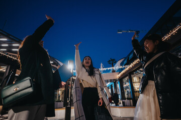 Friends joyfully celebrating under the evening sky, surrounded by light-decorated contemporary...