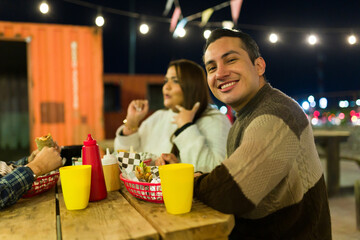 Friends enjoying street food, laughing together near colorful food truck, illuminated by festive evening lights