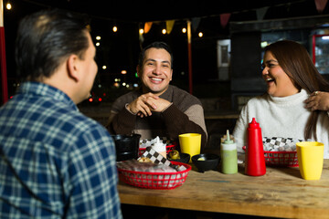 Friends enjoying street food, conversing near illuminated food truck during evening hours