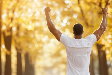 A powerful image of a fit man standing in a sunlit autumn forest with his arms raised in victory.