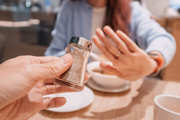 Woman making stop gesture with hand, refusing spices offered by waiter in restaurant