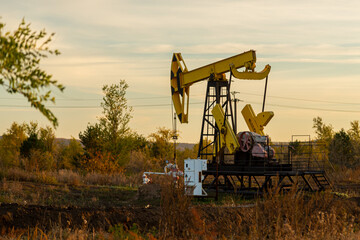 Oil well drilling rig in the middle of autumn field on a clear evening sunset